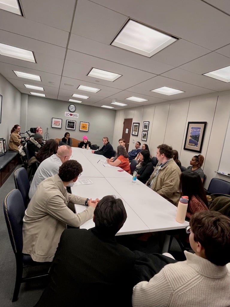 A large group of people seated around a conference table in a congressional meeting room.