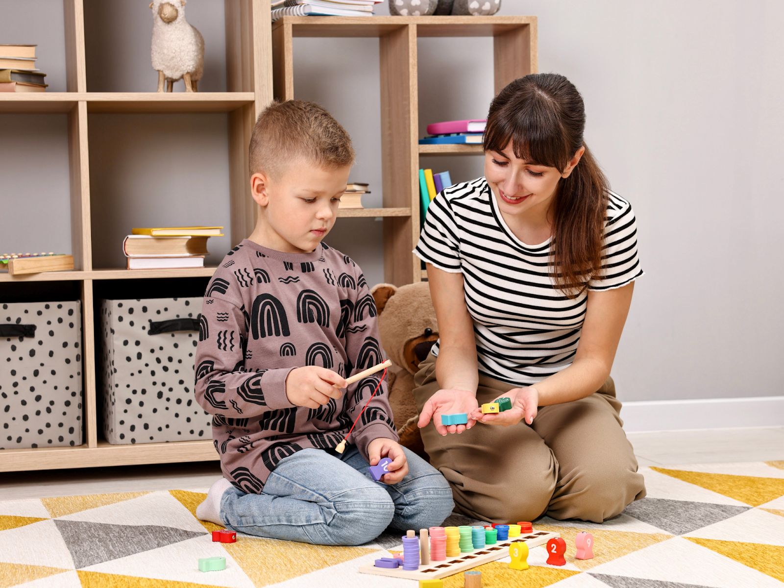 A young boy and a woman kneeling on the floor and playing with colorful toys.