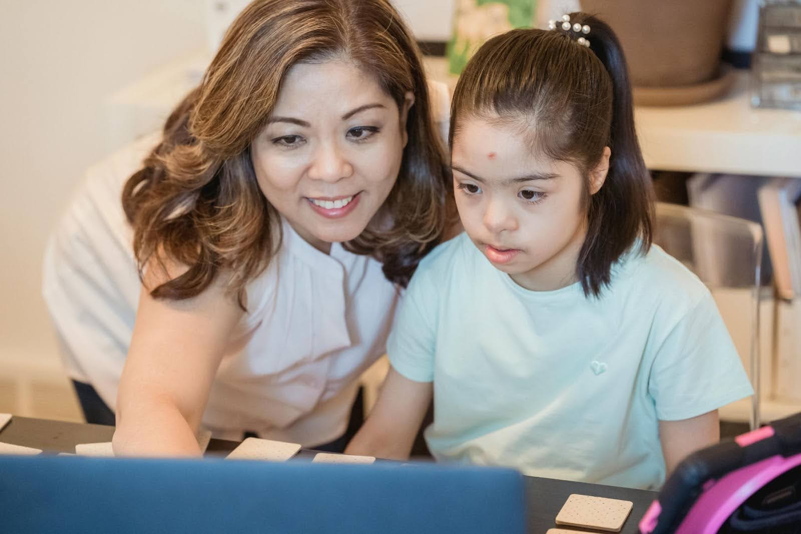 A mother and her daughter with Down Syndrome sit side by side and explore information together on a computer
