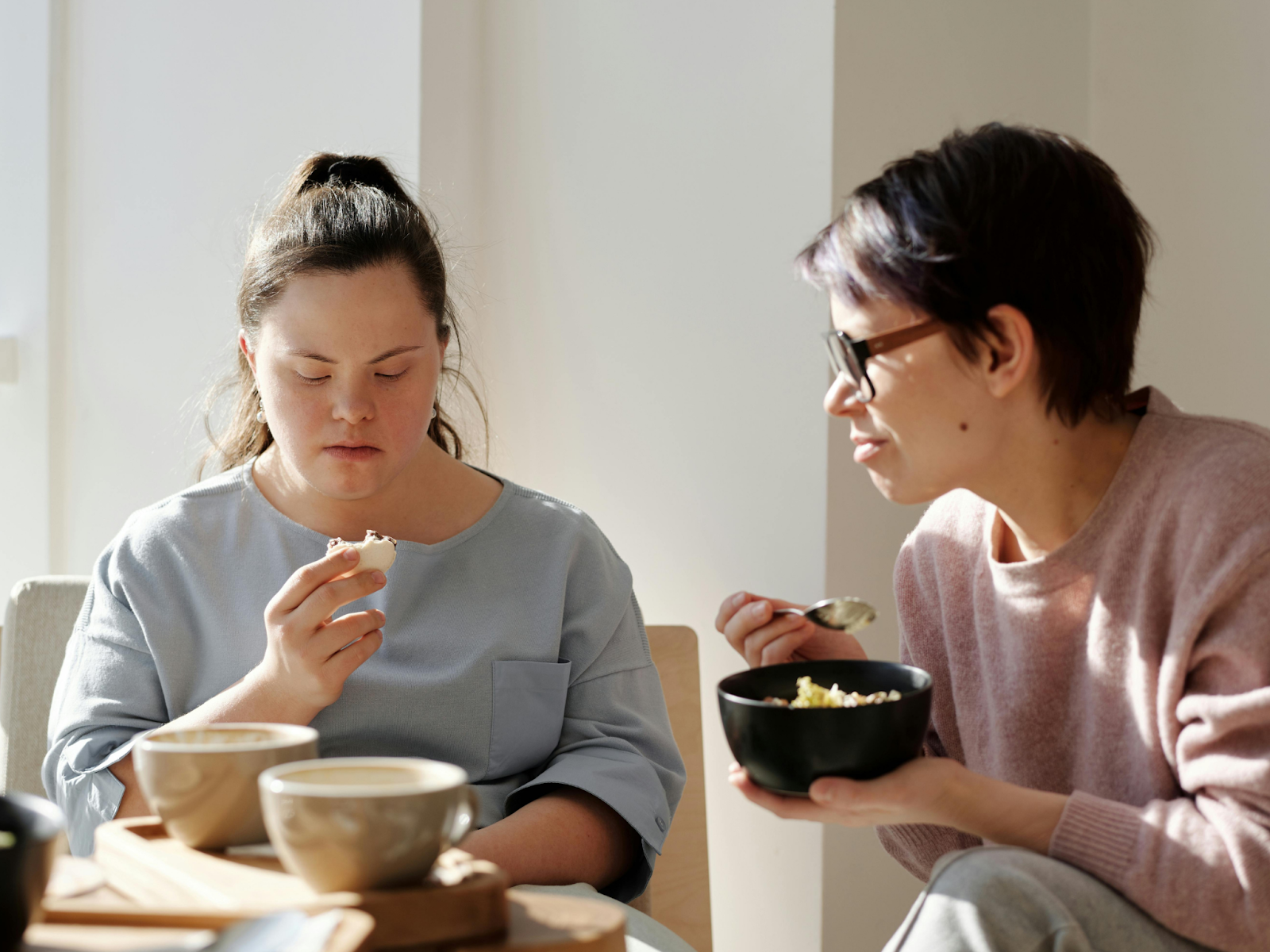 A woman with Down syndrome and her caregiver sitting together and eating.