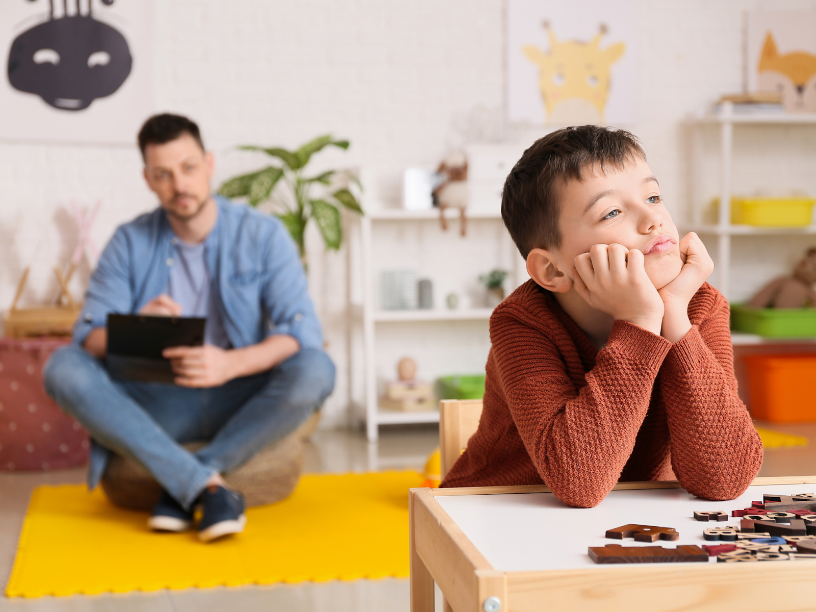 A man taking notes as a boy leans on a table and looks away from him.