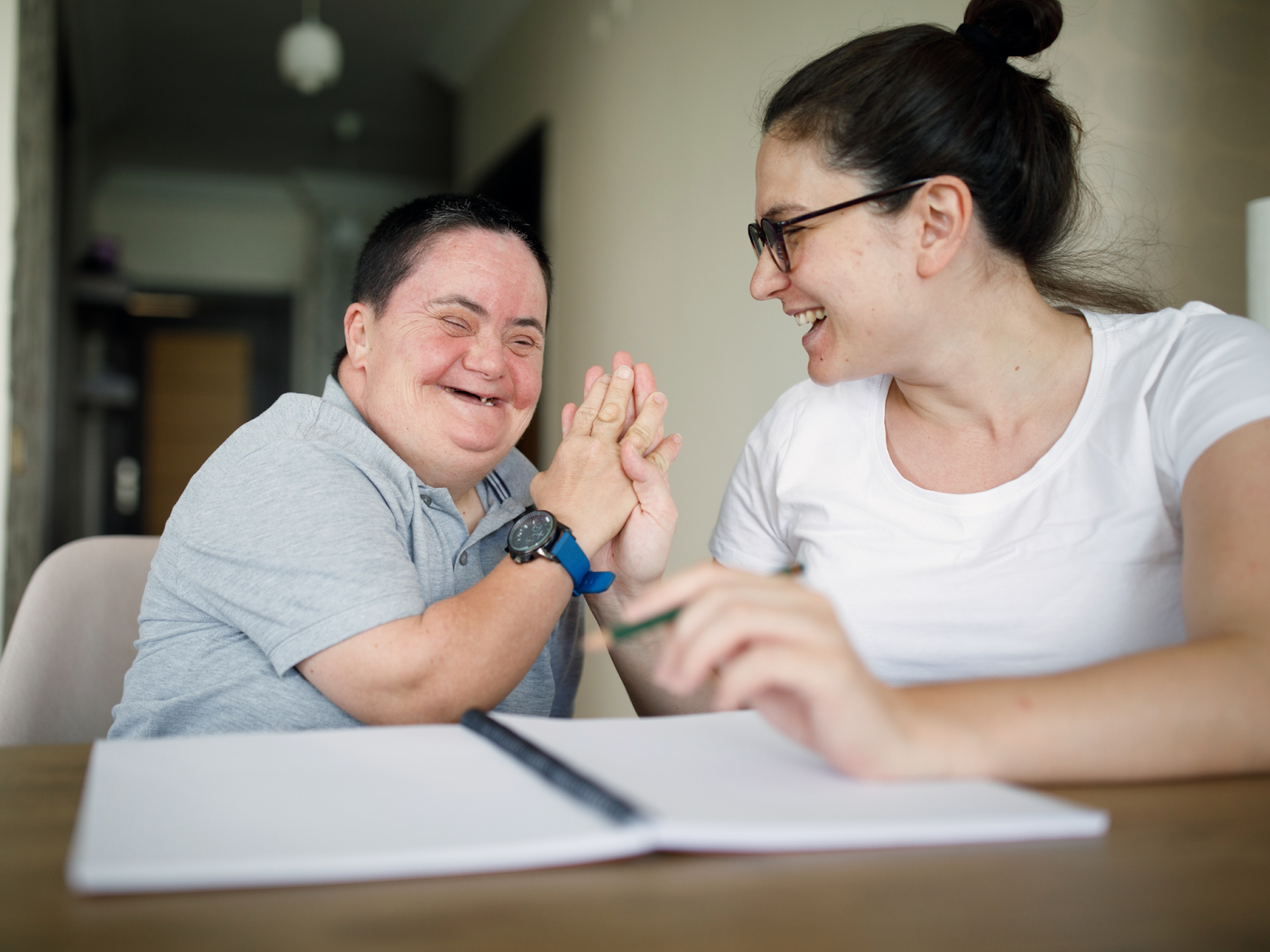 A person with a disability and a support staff member smiling and high-fiving.