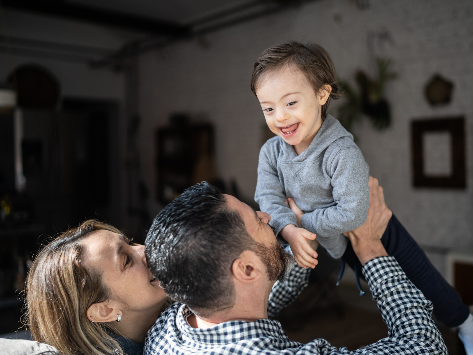 Two parents lifting their disabled child over their heads as he smiles.
