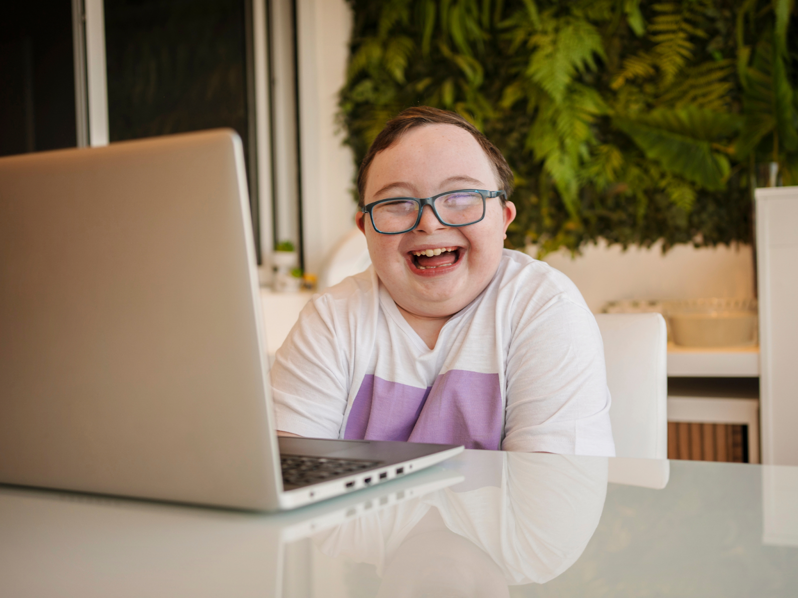 A child with Down syndrome sitting in front of a laptop and smiling.