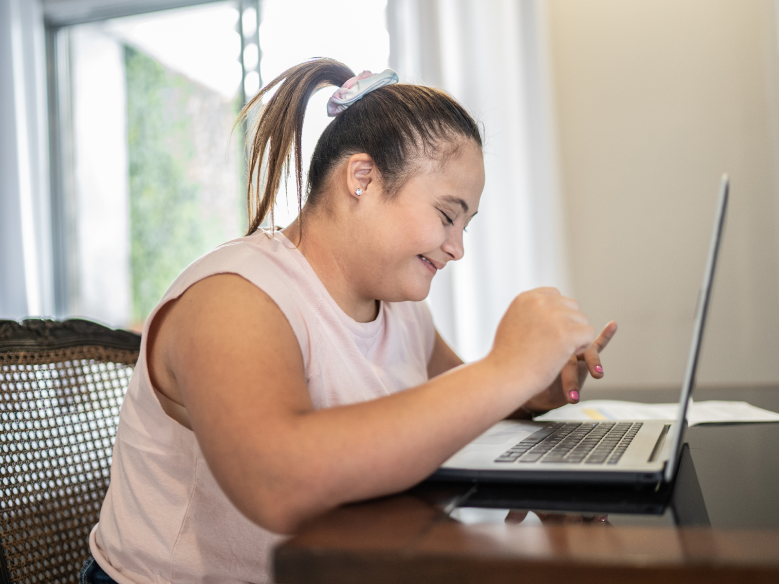 A girl with Down syndrome smiling while doing homework on a laptop.
