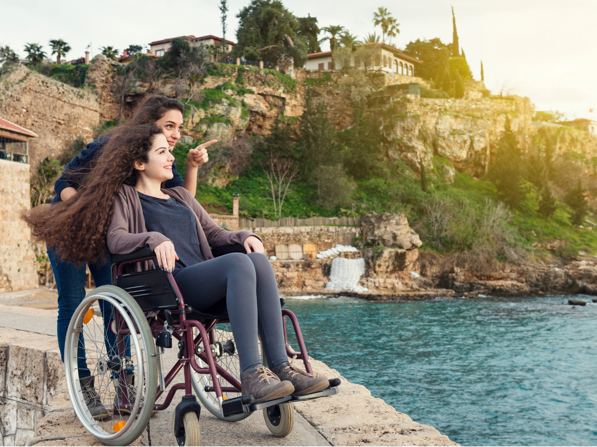 Two women, one in a wheelchair, smiling and looking over the ocean