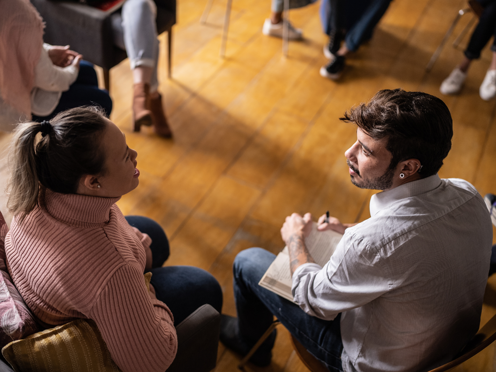 A woman with a disability sitting and speaking to a man holding an open book.