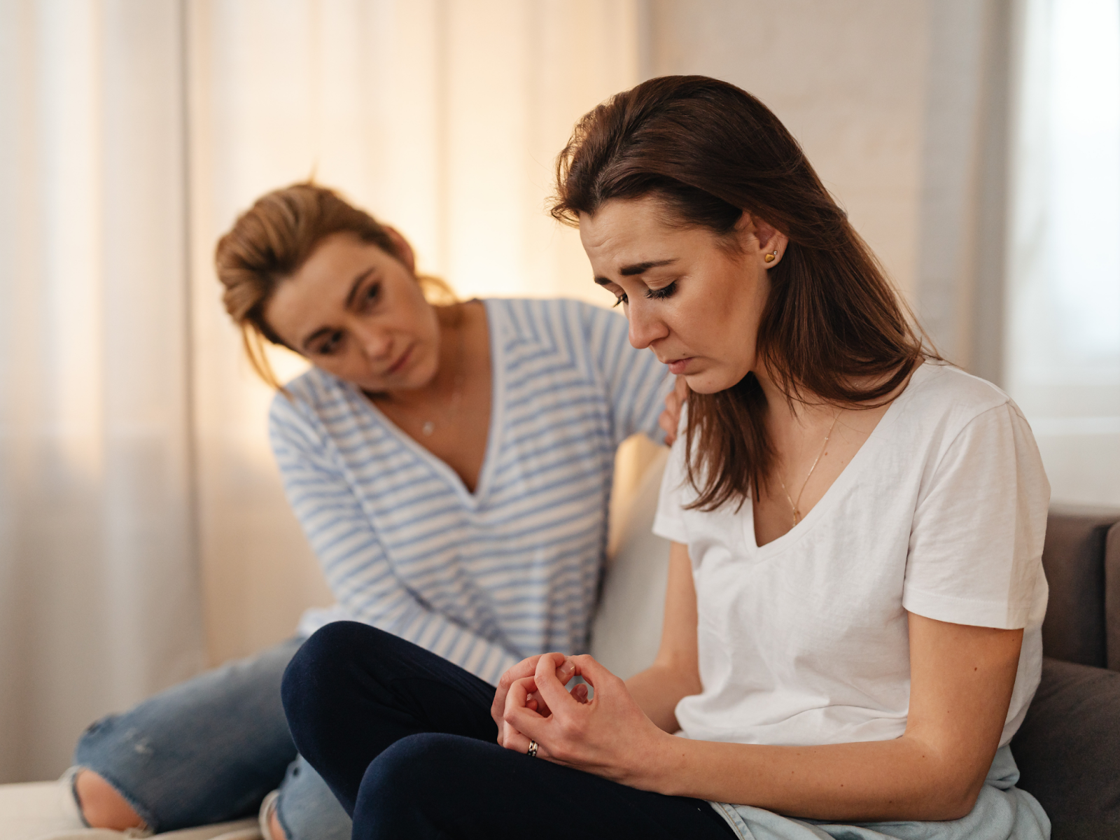 A woman looking down sadly while another woman comforts her.