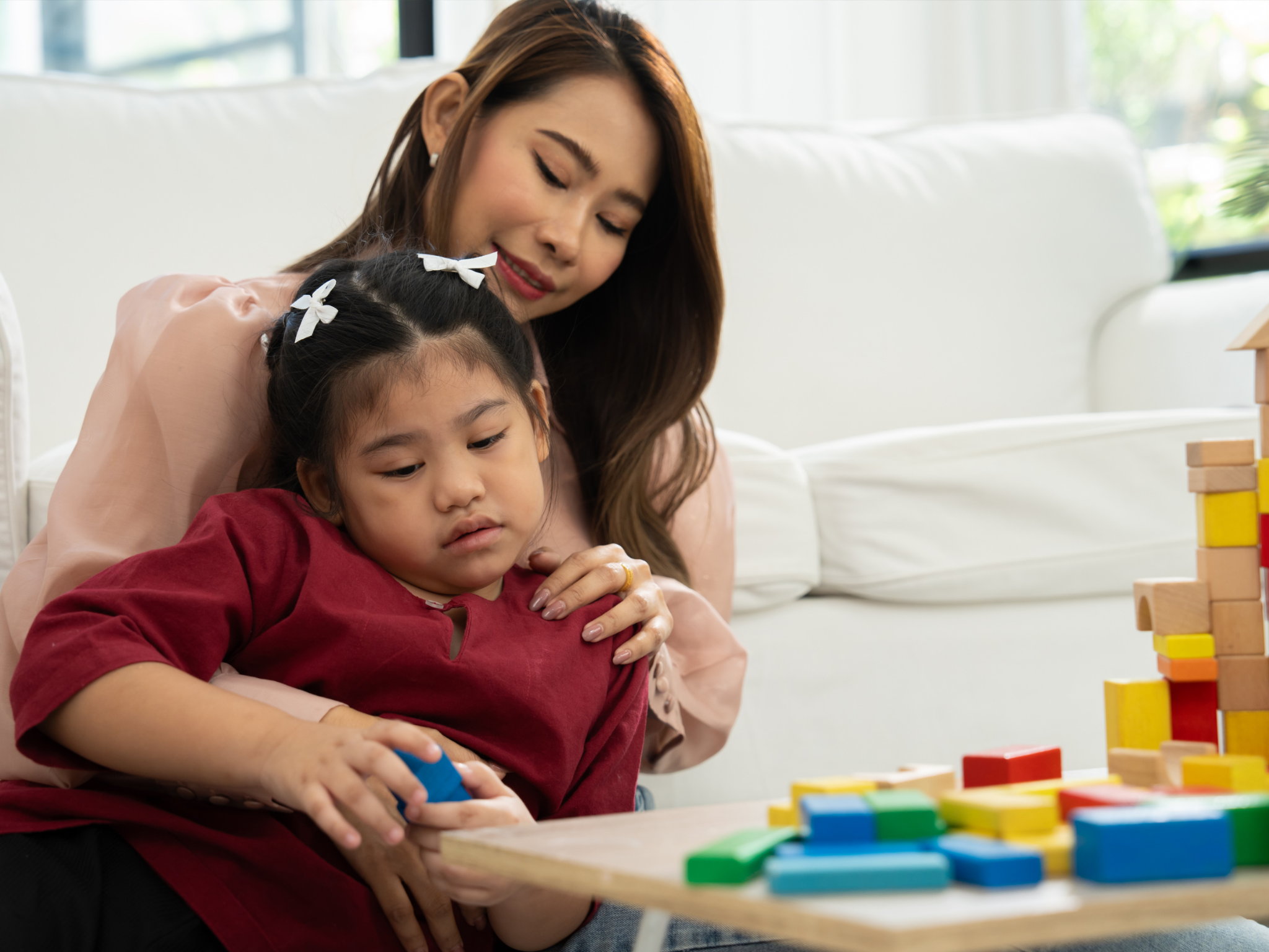 A mother holds her daughter on her lap as they play with colorful blocks.