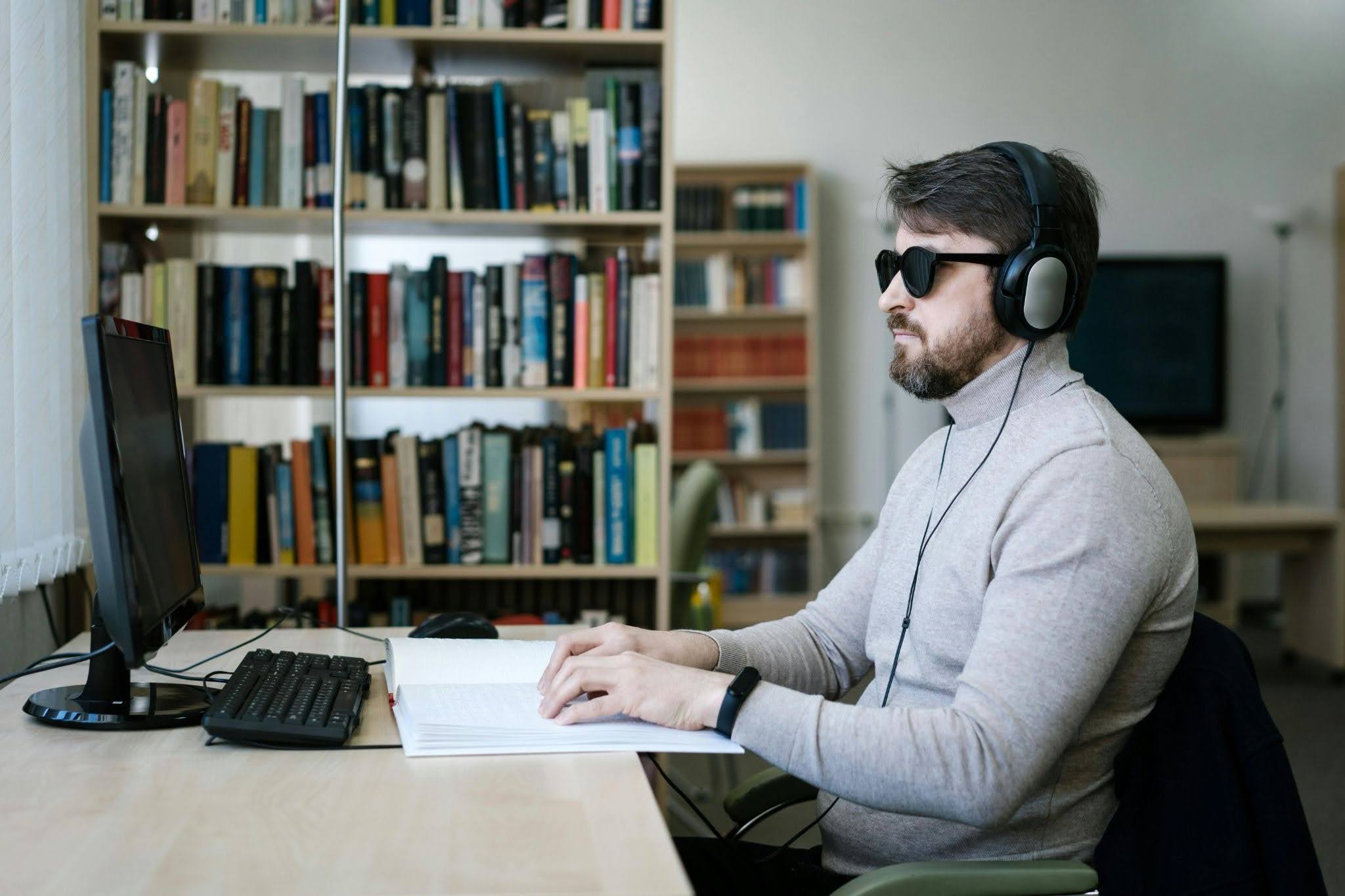 A blind man wearing a headset while using Braille to listen to and read digital content from a computer