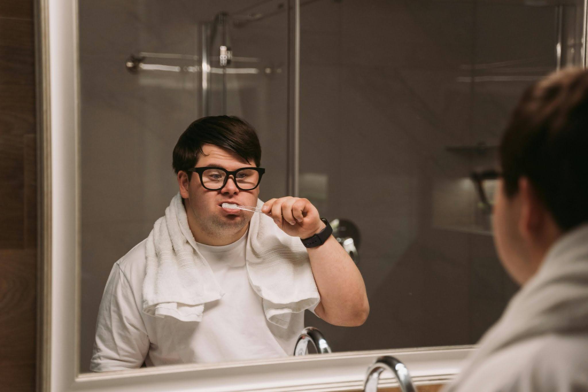 An autistic person brushing their teeth while looking in a bathroom mirror.