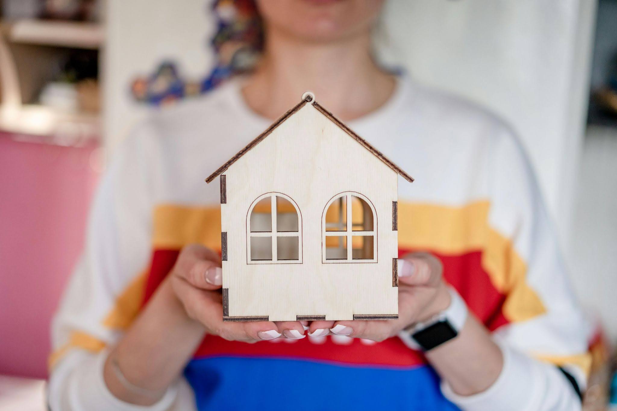 An out-of-focus person holds a wooden model house