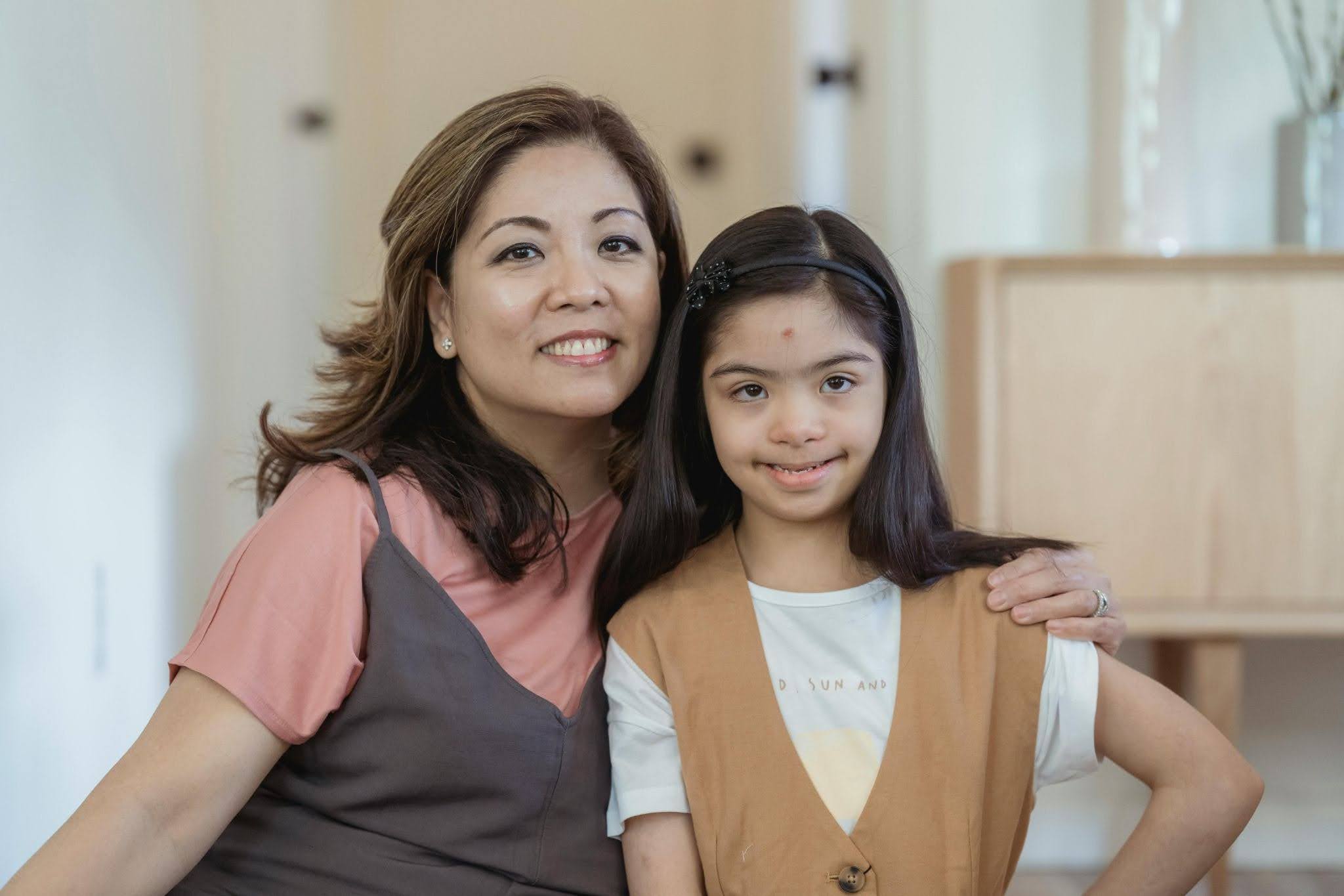 A mother and her daughter with Down Syndrome stand next to each other and smile