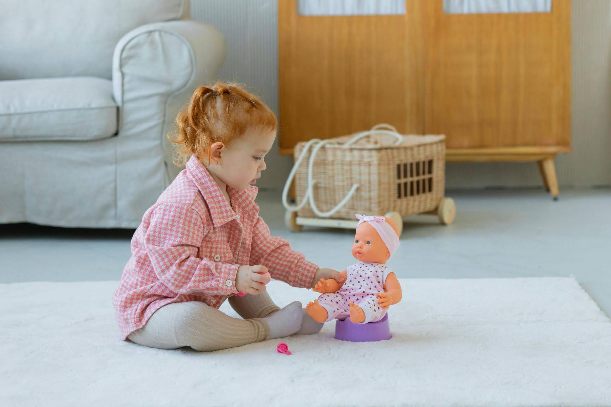 A young girl playing with a doll on a toy potty.