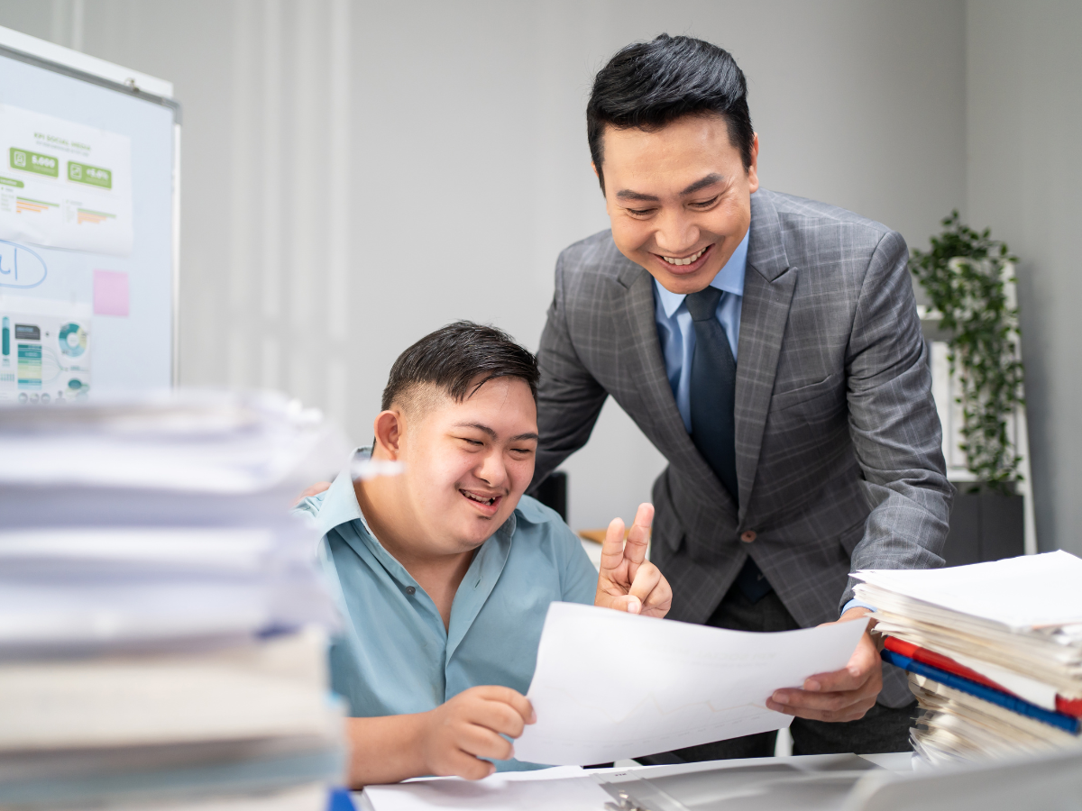 A boss and an employee with disabilities look at a piece of paper together and smile