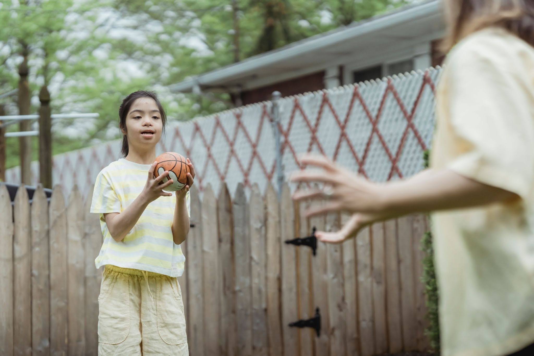 A young girl with autism plays catch with a ball.