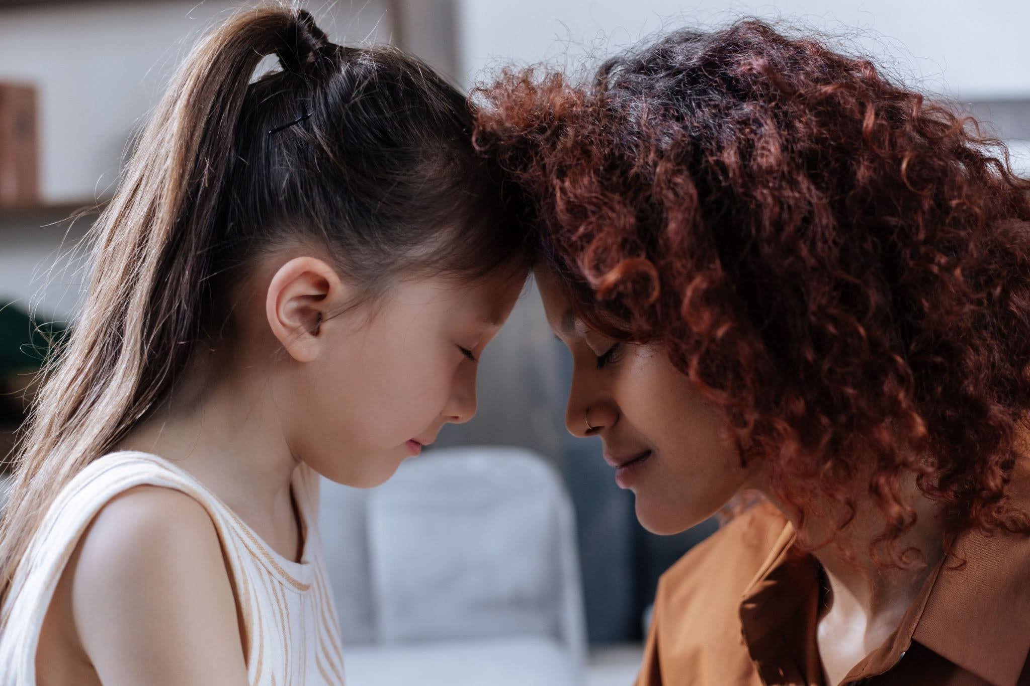 A mom and her daughter touch foreheads and smile in a moment of connection