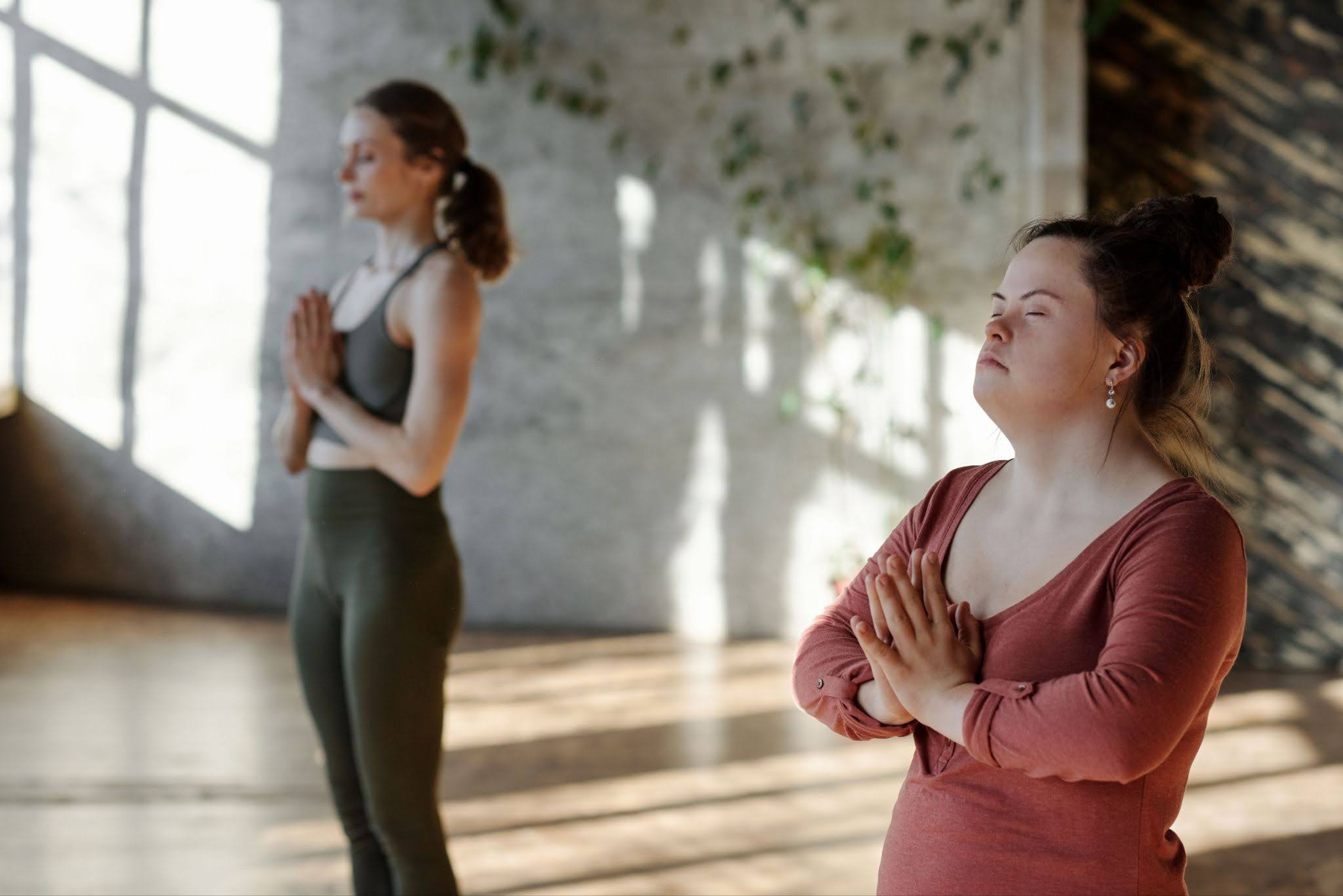 Two people participate in yoga at a studio filled with natural light