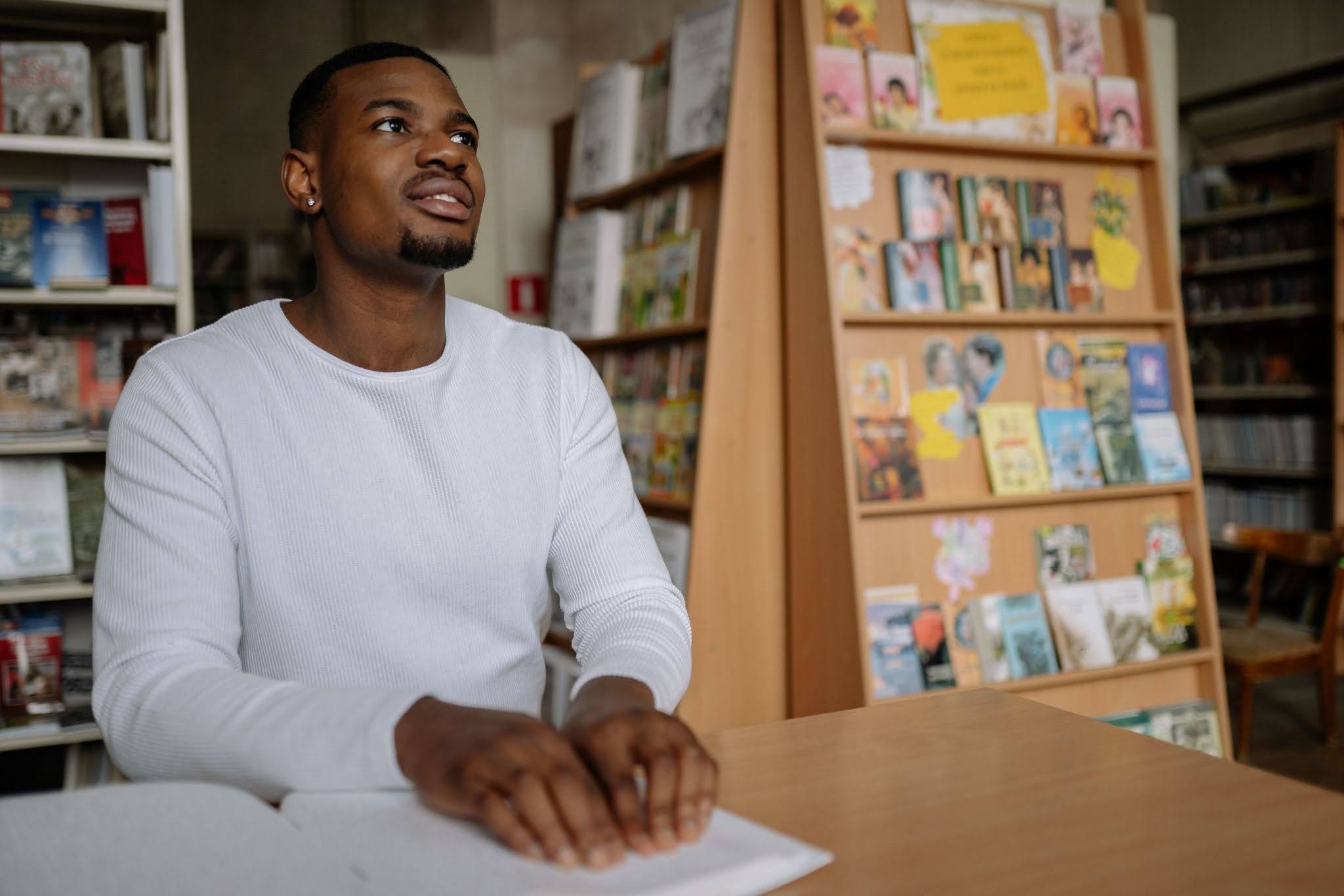A man sits at a table at his local library and reads a book in Braille