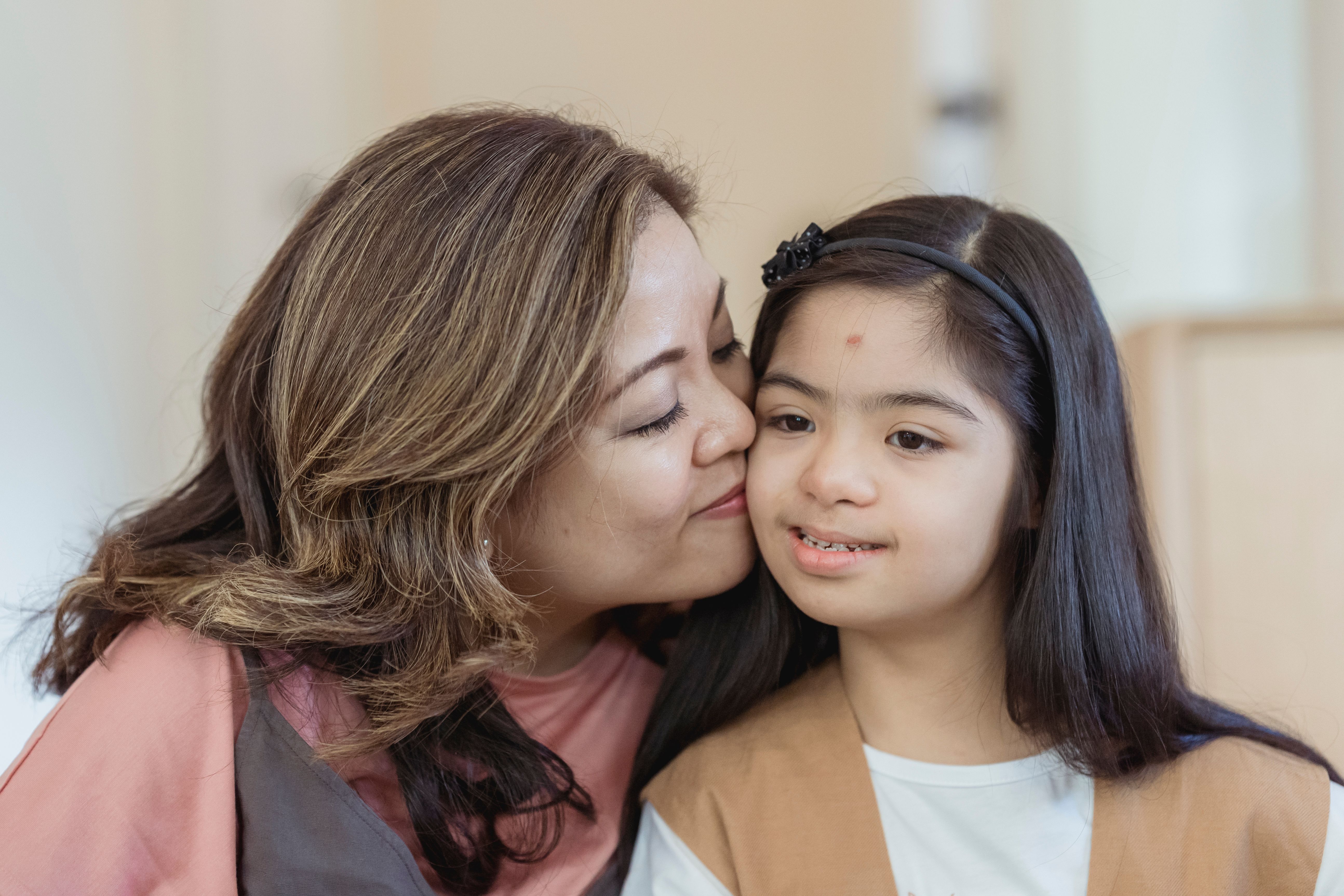 A mother of a girl with Down syndrome kisses her daughter on the cheek