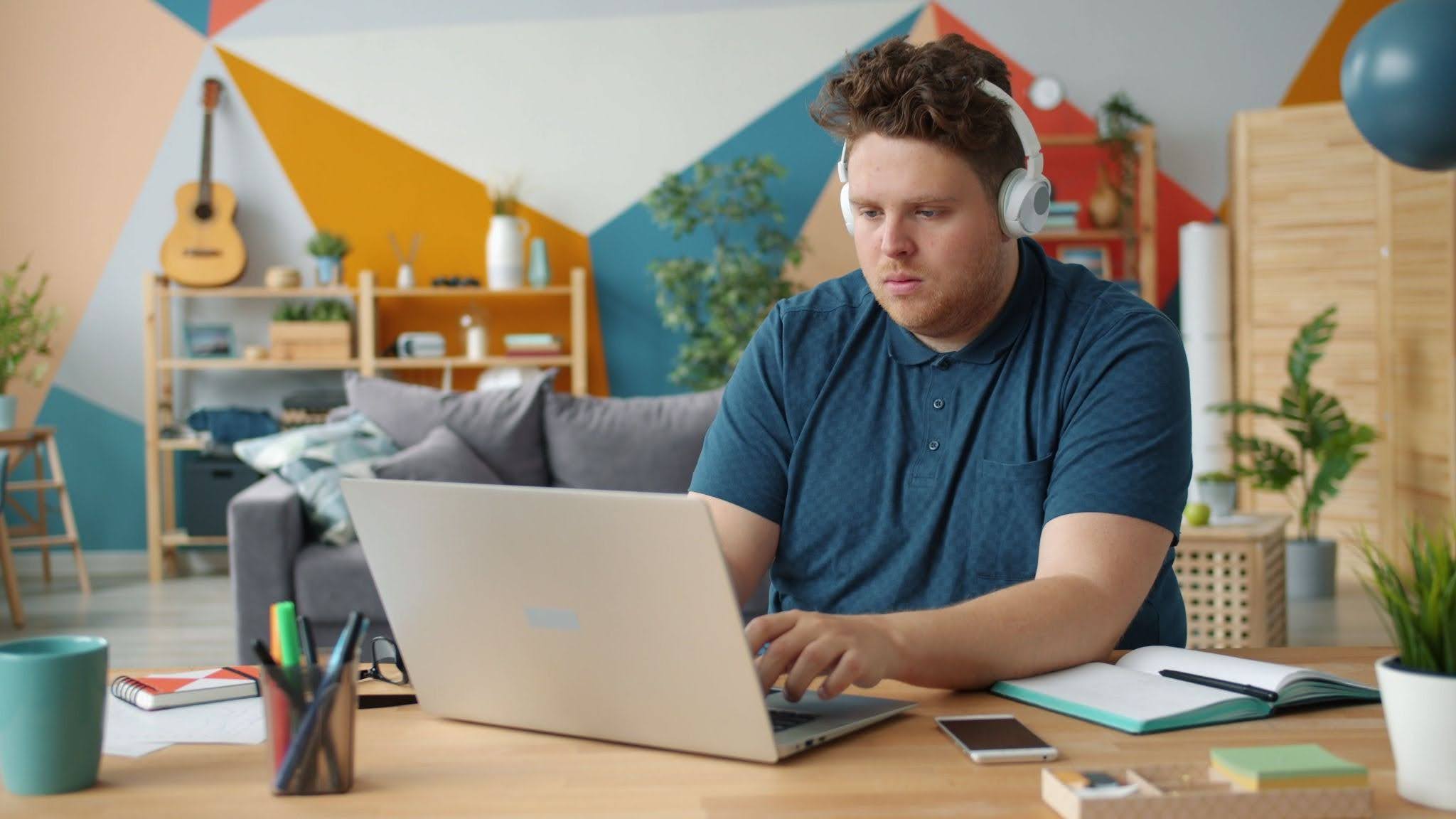 A man with ADHD wears headphones while working on his laptop