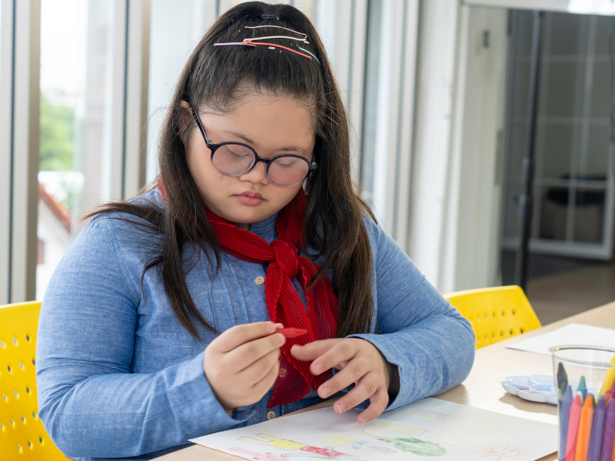 A woman sitting at a desk and drawing with crayons