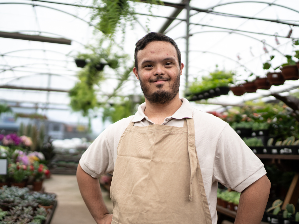 A man with Down syndrome smiling and standing in a greenhouse with plants