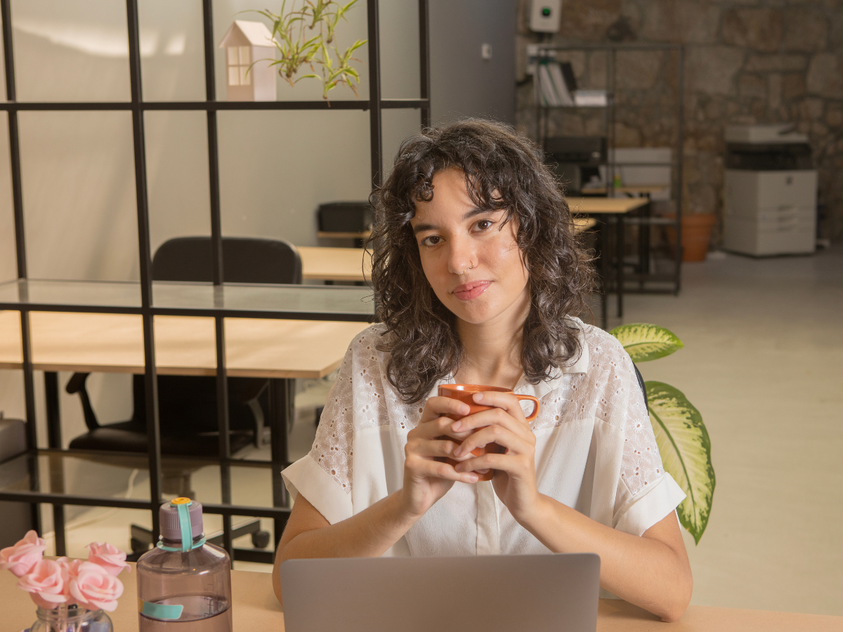 Woman facing forward holding a mug and sitting at office desk with laptop