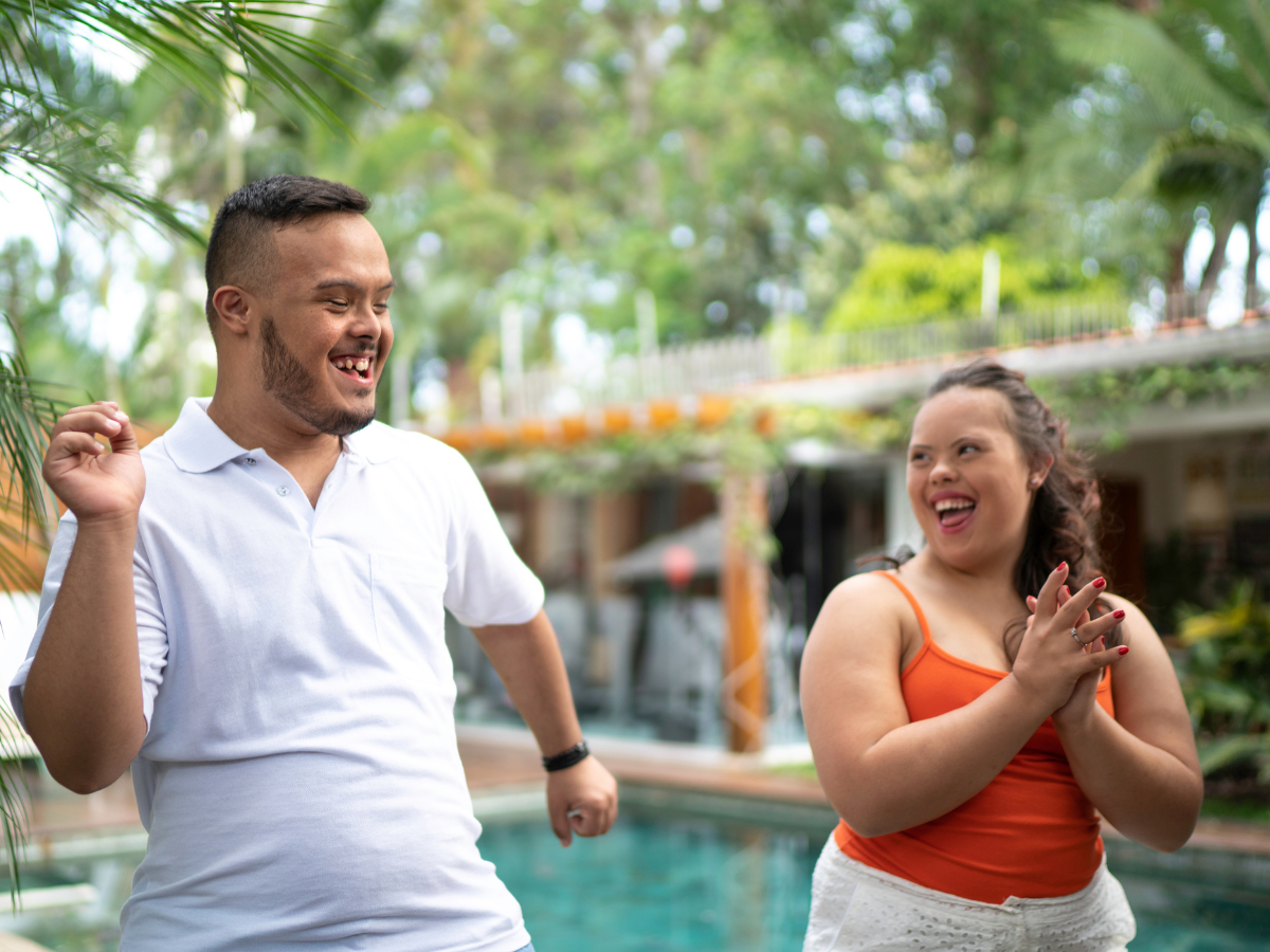 Two adults with disabilities exercising and dancing by a pool while smiling