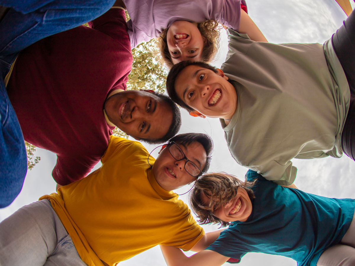 Five people with their arms around each other and heads together, smiling