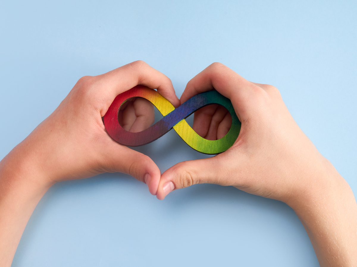 Two hands forming a heart with a rainbow infinity symbol inside