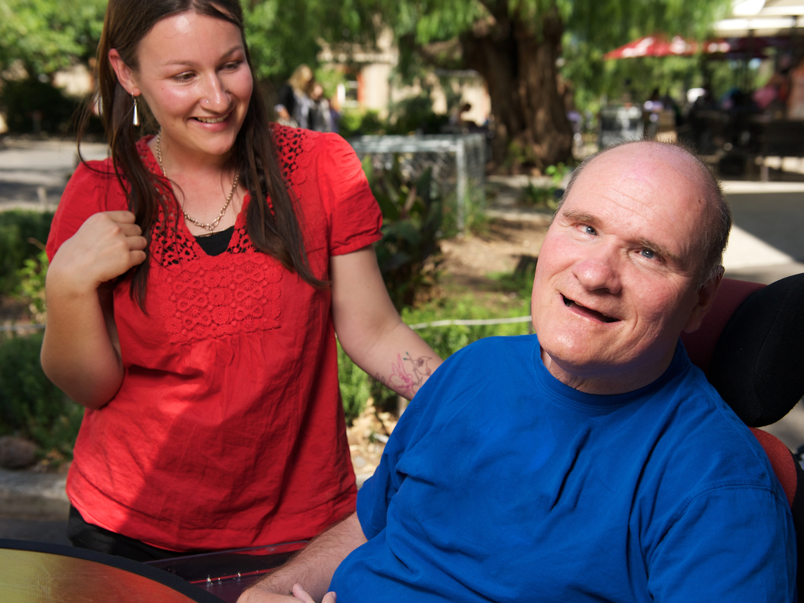 A smiling caretaker with an adult with a disability in a wheelchair outdoors