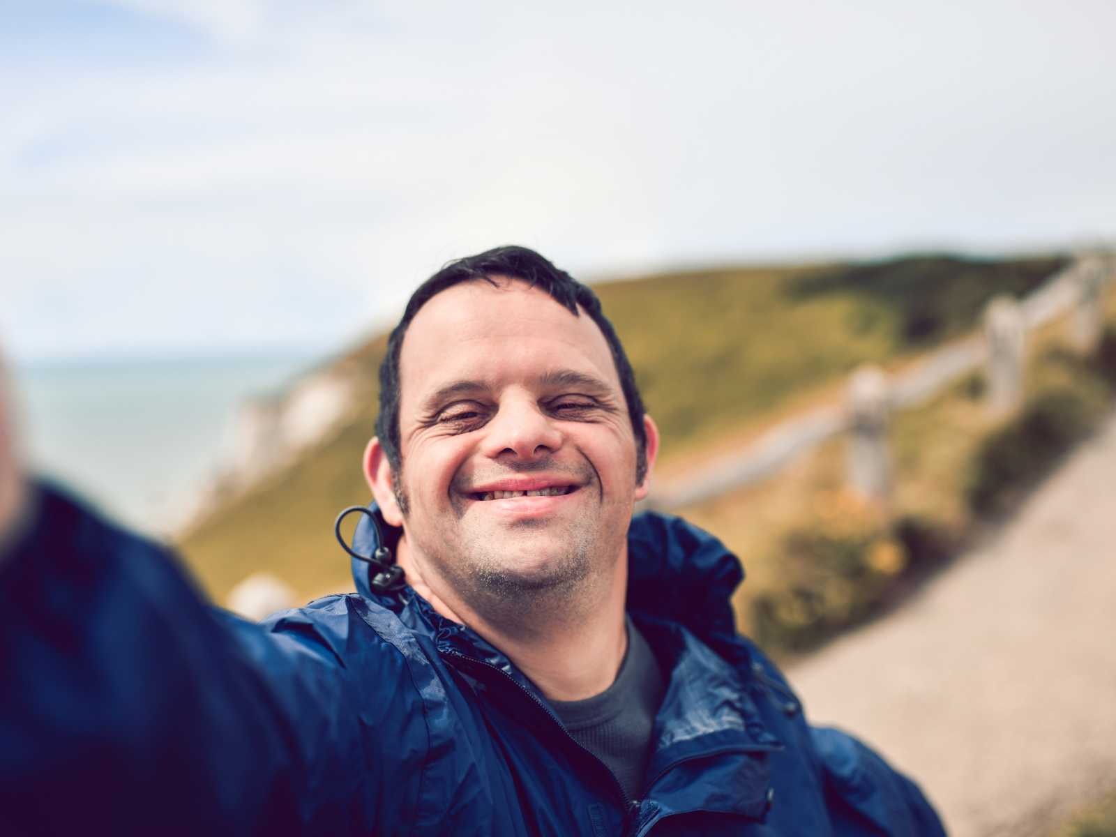 An adult with a disability smiling and taking a selfie outdoors