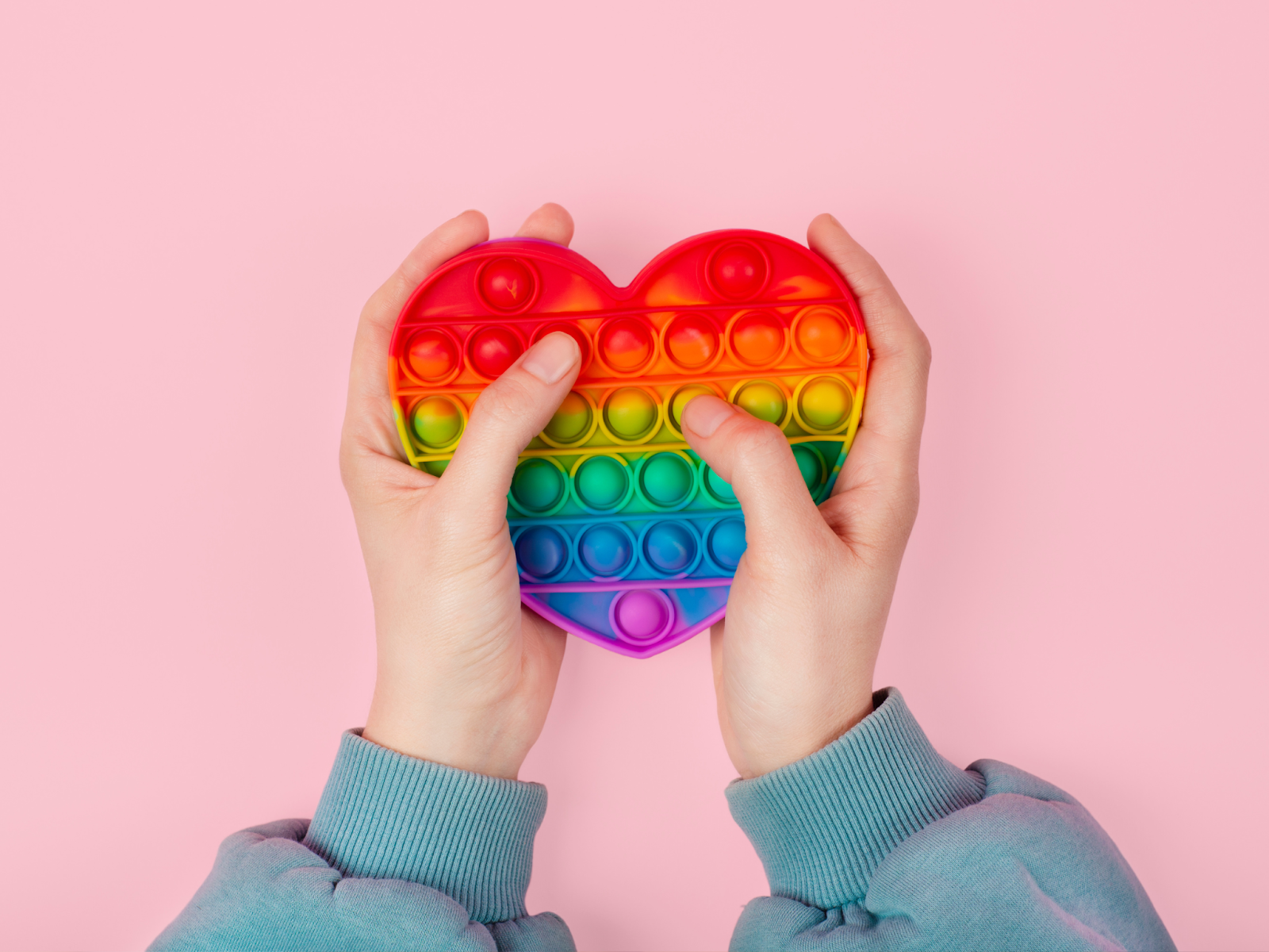 Two hands holding a colorful fidget toy over a pink background