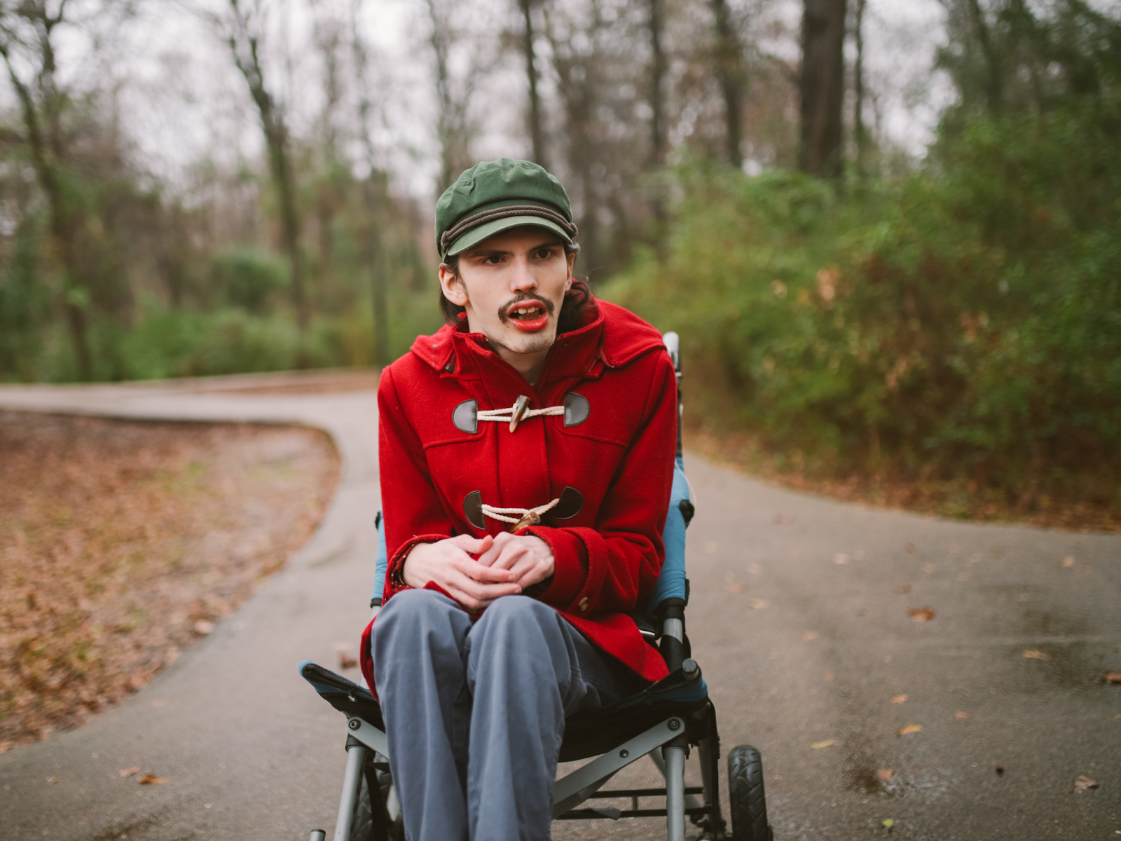 A person sits in their wheelchair on an outdoor paved walking track