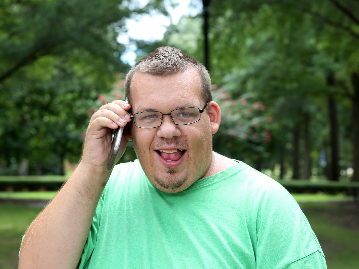 Man in green shirt active listening on cell phone in a public setting