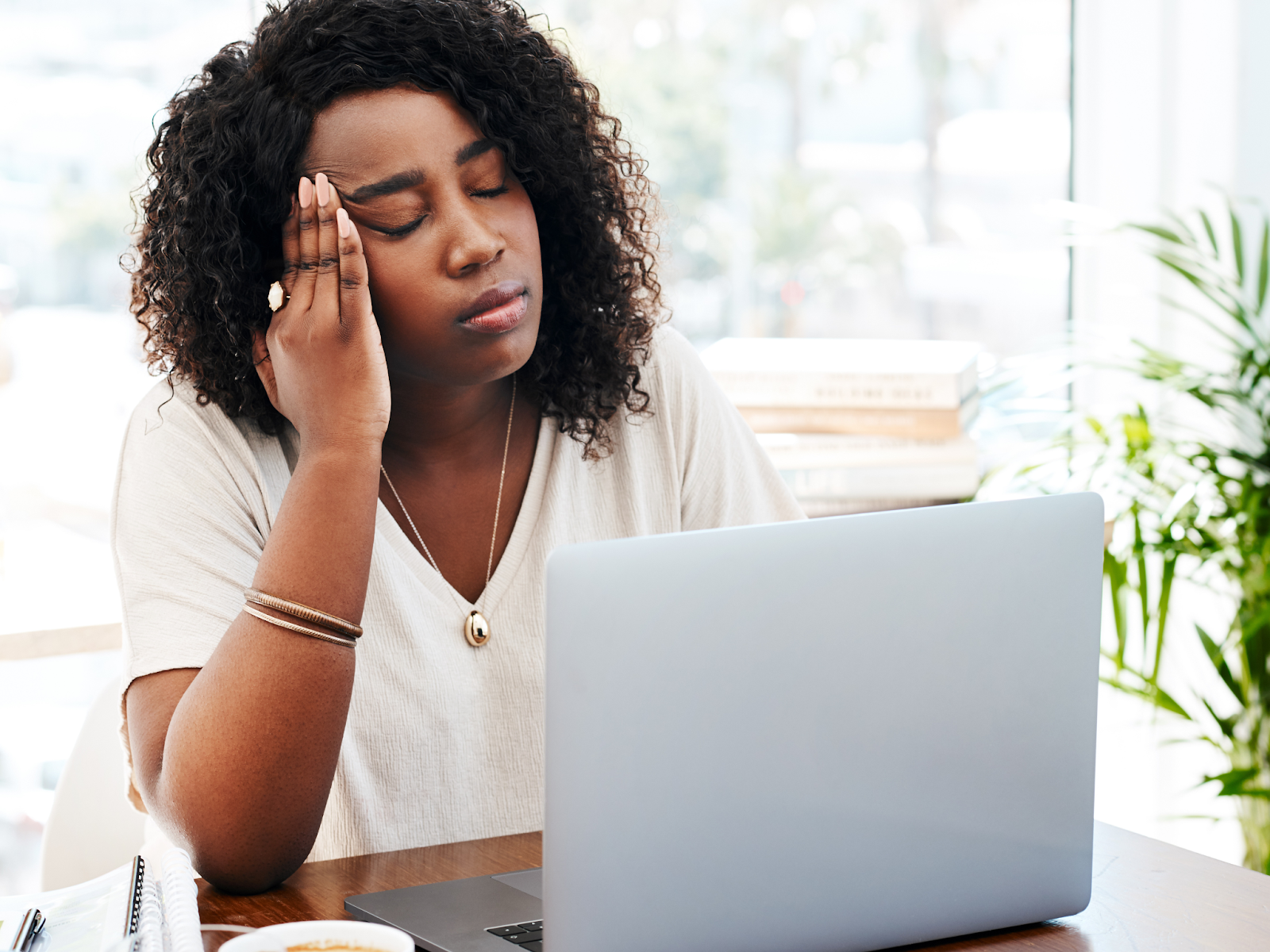 An adult in front of a laptop rubbing their temple with their eyes closed