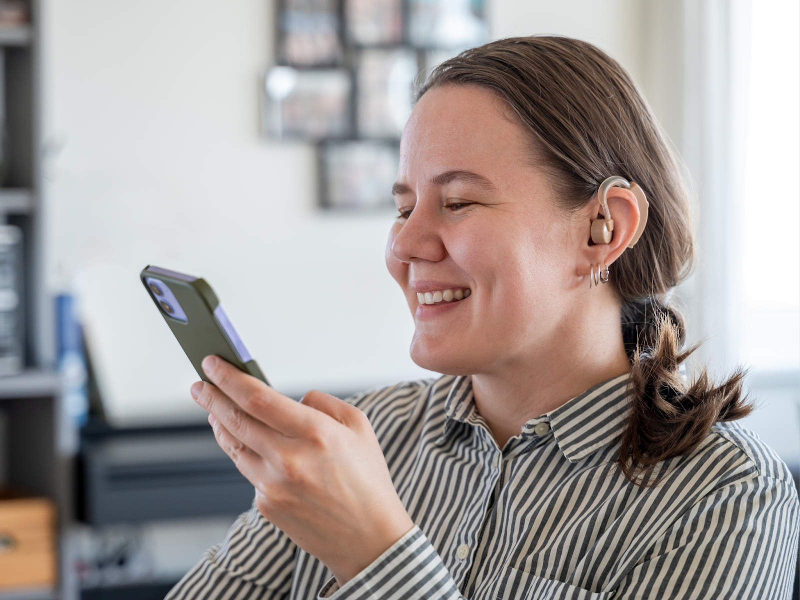 A hard of hearing adult with a hearing aid smiling at a cell phone