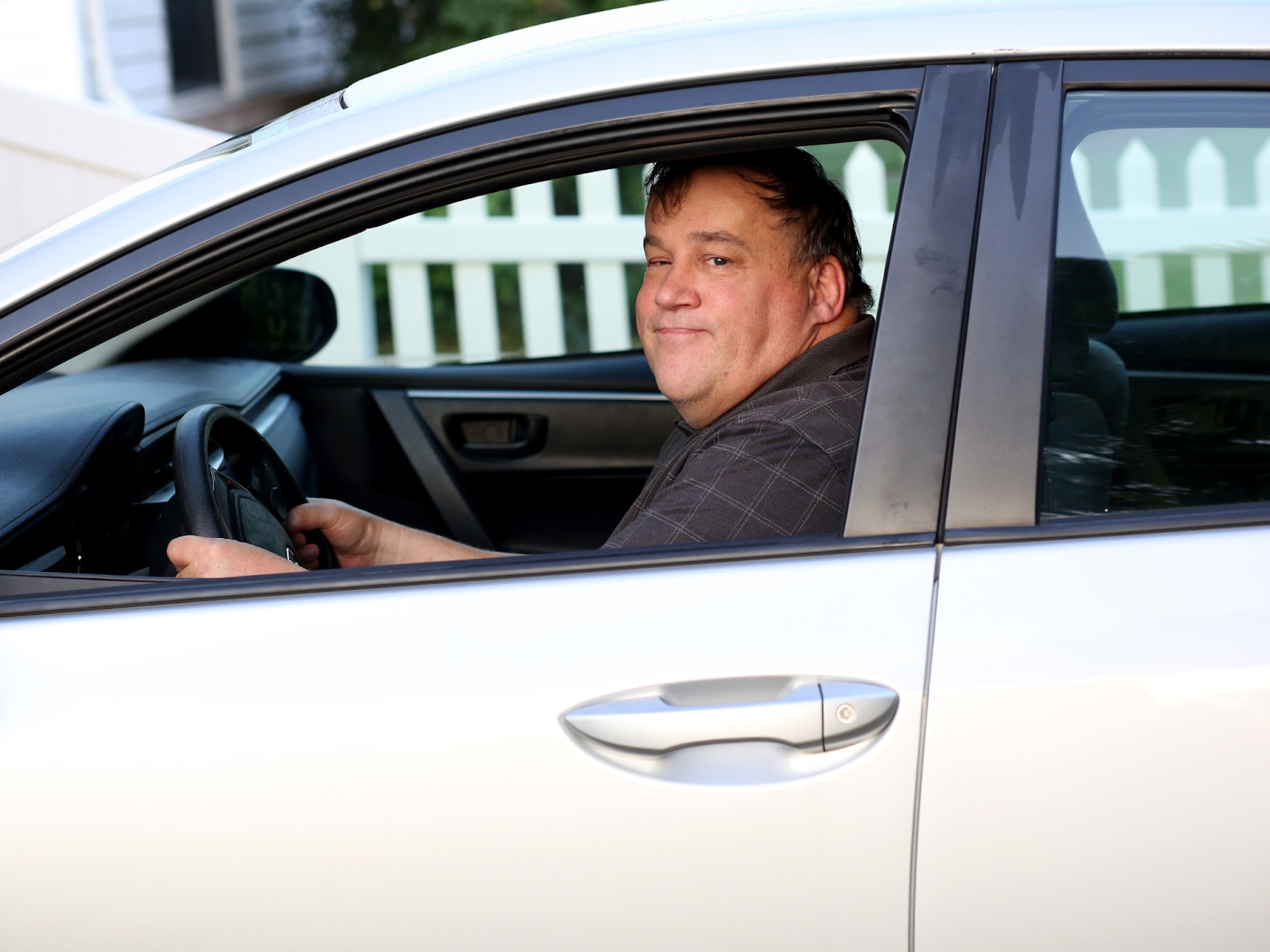 An autistic adult drives his car and smiles while looking out the side window.