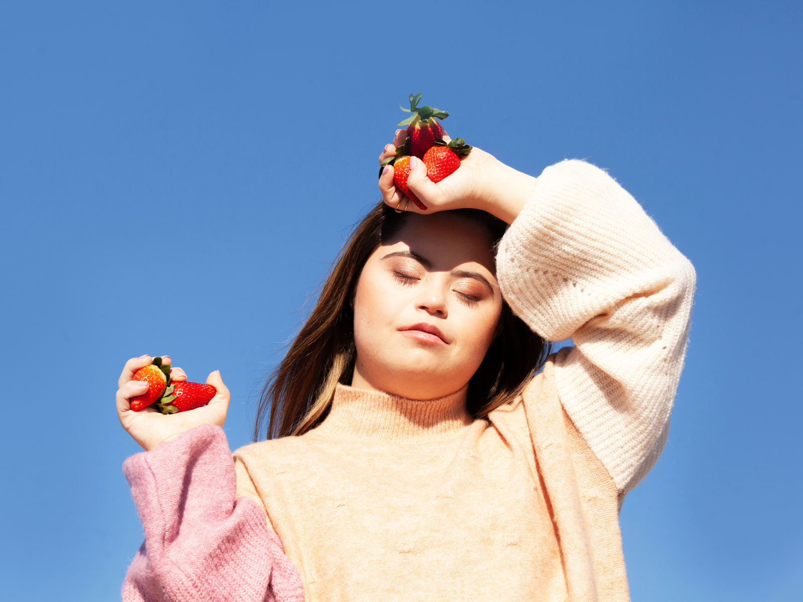 A young woman with Down Syndrome posing while holding strawberries in front of a clear blue sky.
