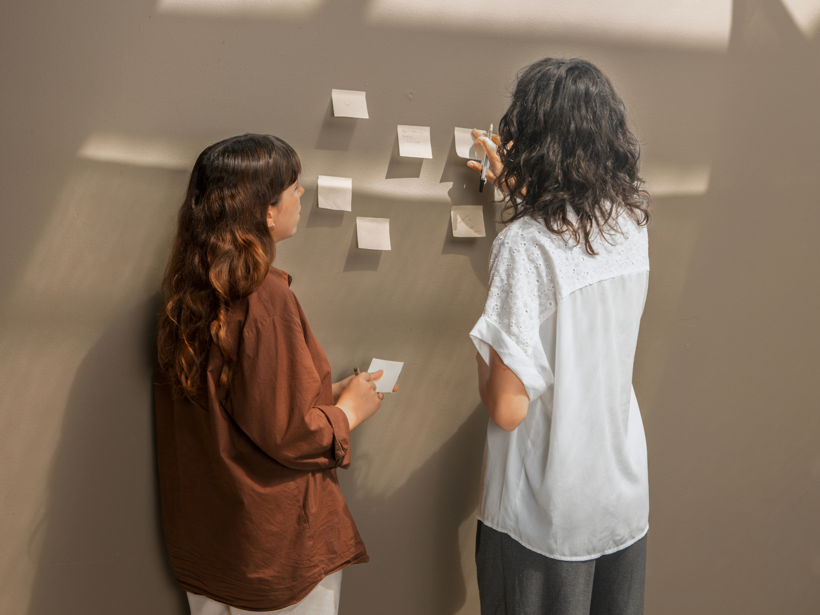 Two adults facing a wall with post-it notes stuck to it.