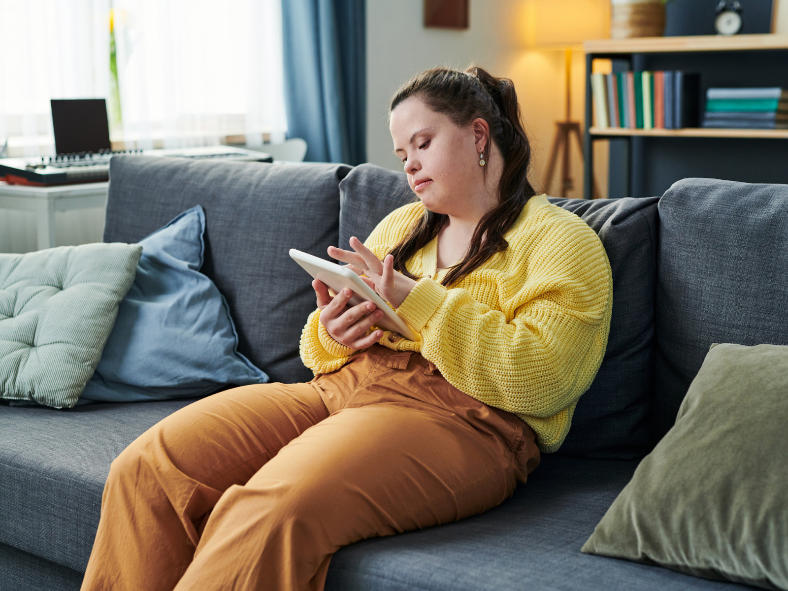 An adult with Down syndrome sitting on a couch and using a tablet.