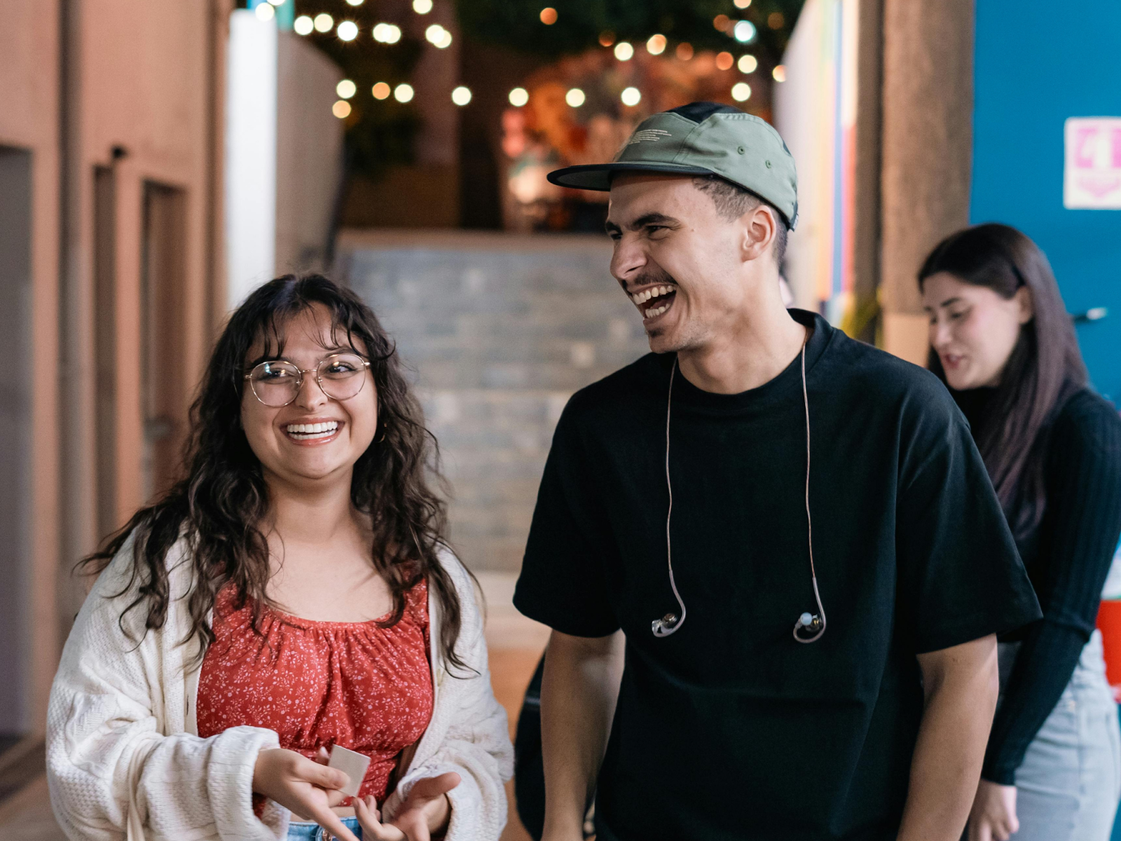 An autistic adult and a friend stand together laughing and smiling while standing in a hallway.