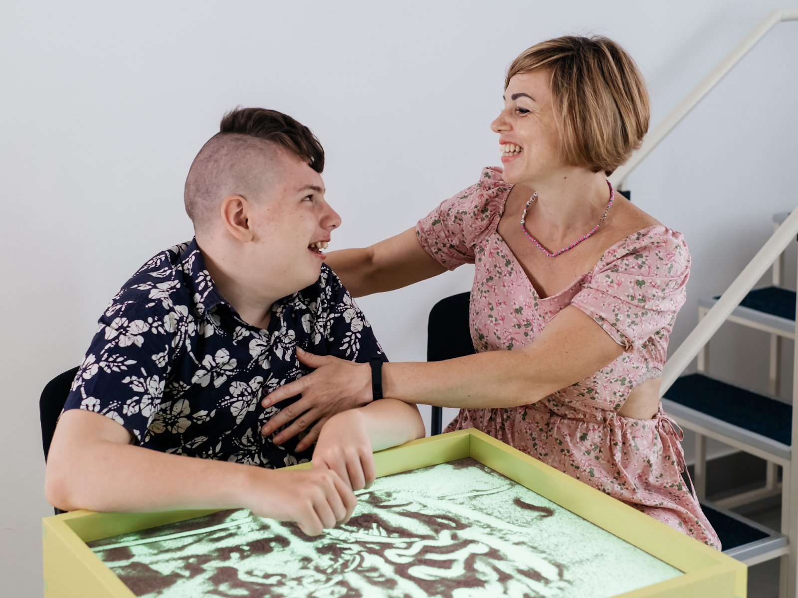 A person with autism sitting at a sand table with a therapist.