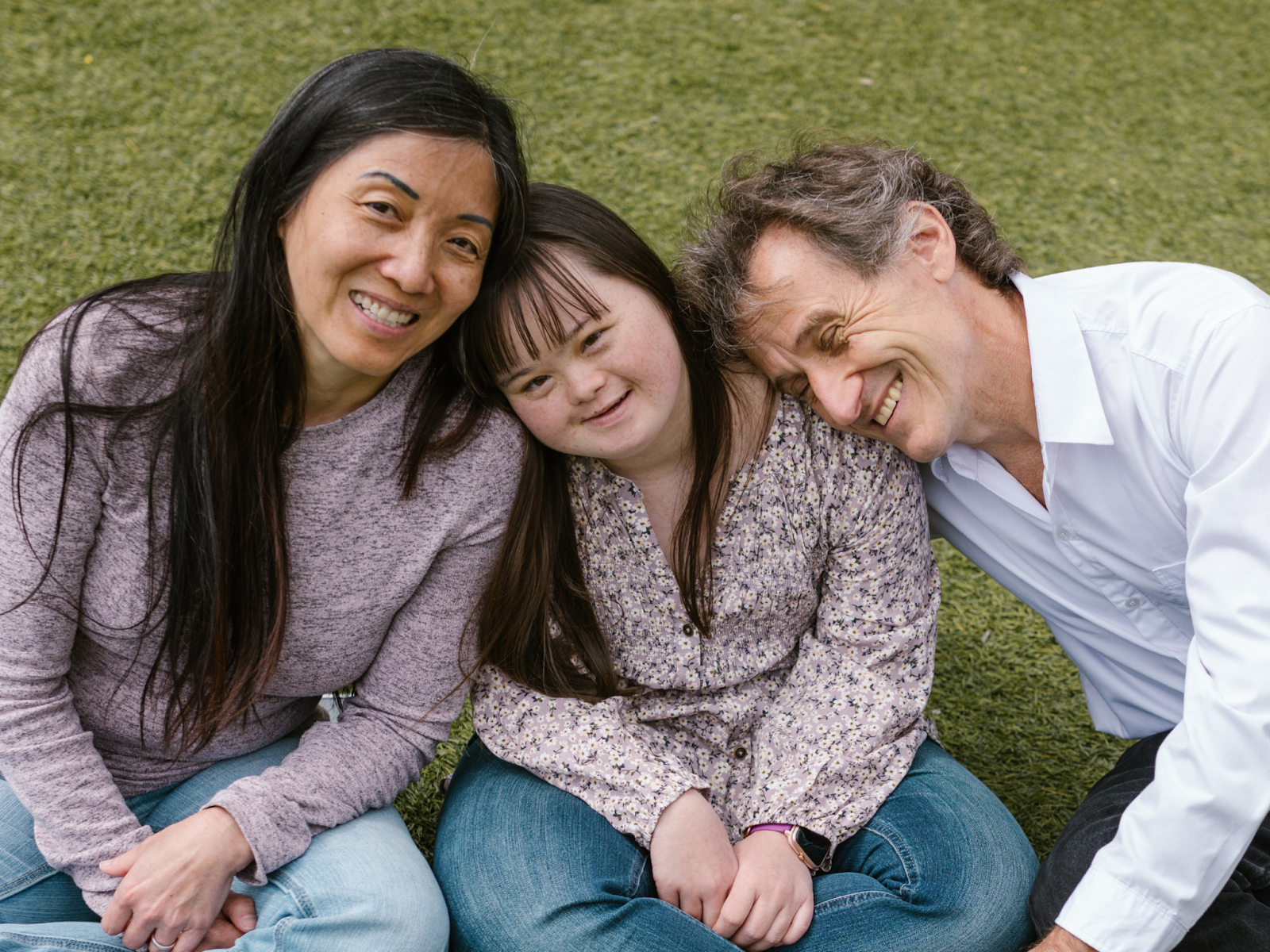 A mother, daughter, and father sitting in the grass and smiling.