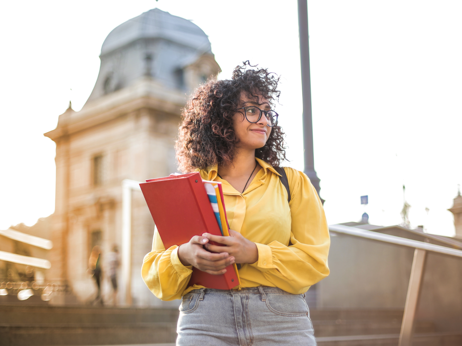 A smiling college student standing outdoors and holding a red binder and colorful folders.