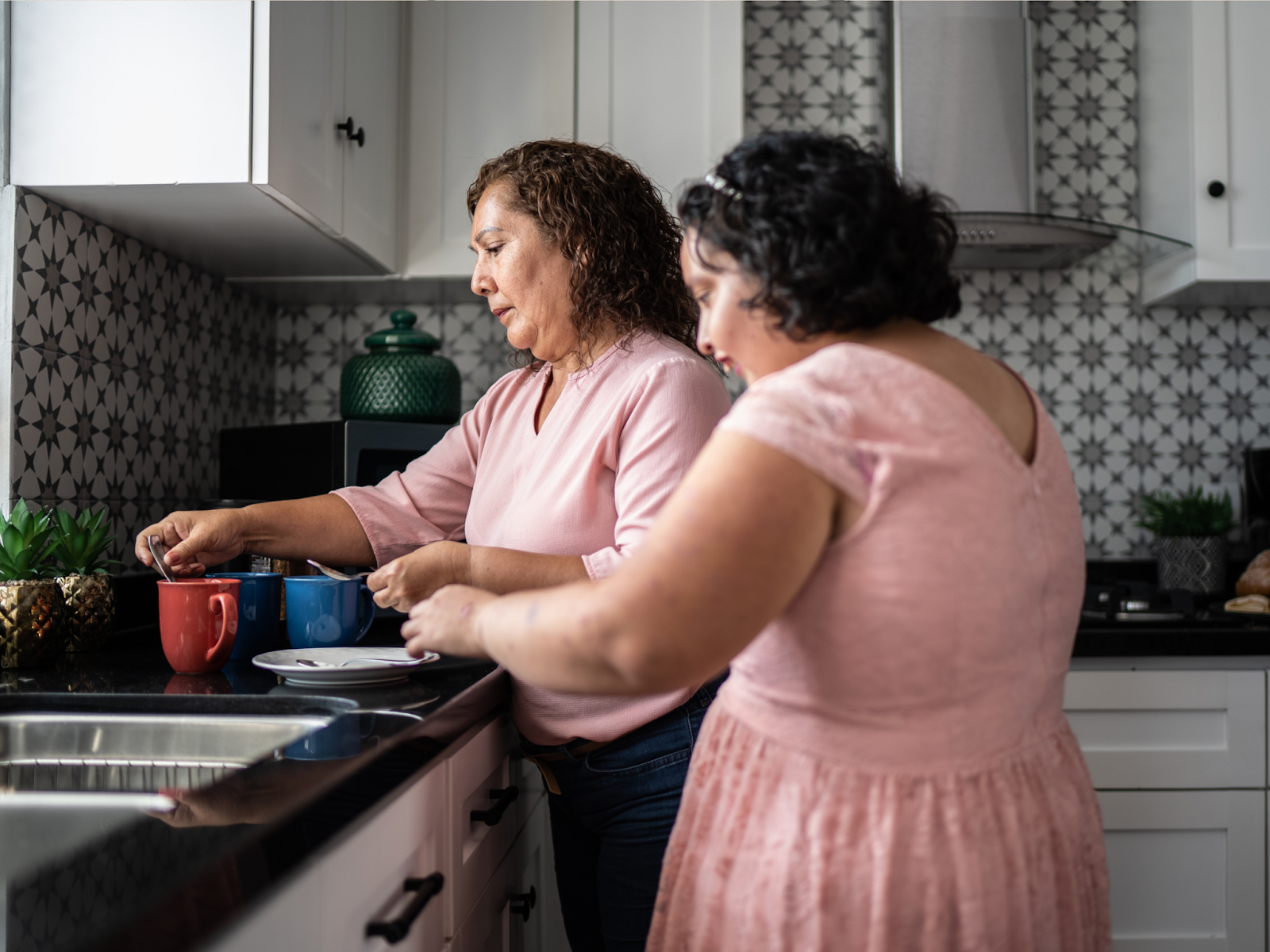 A mother and daughter standing in a kitchen preparing drinks in colorful mugs.