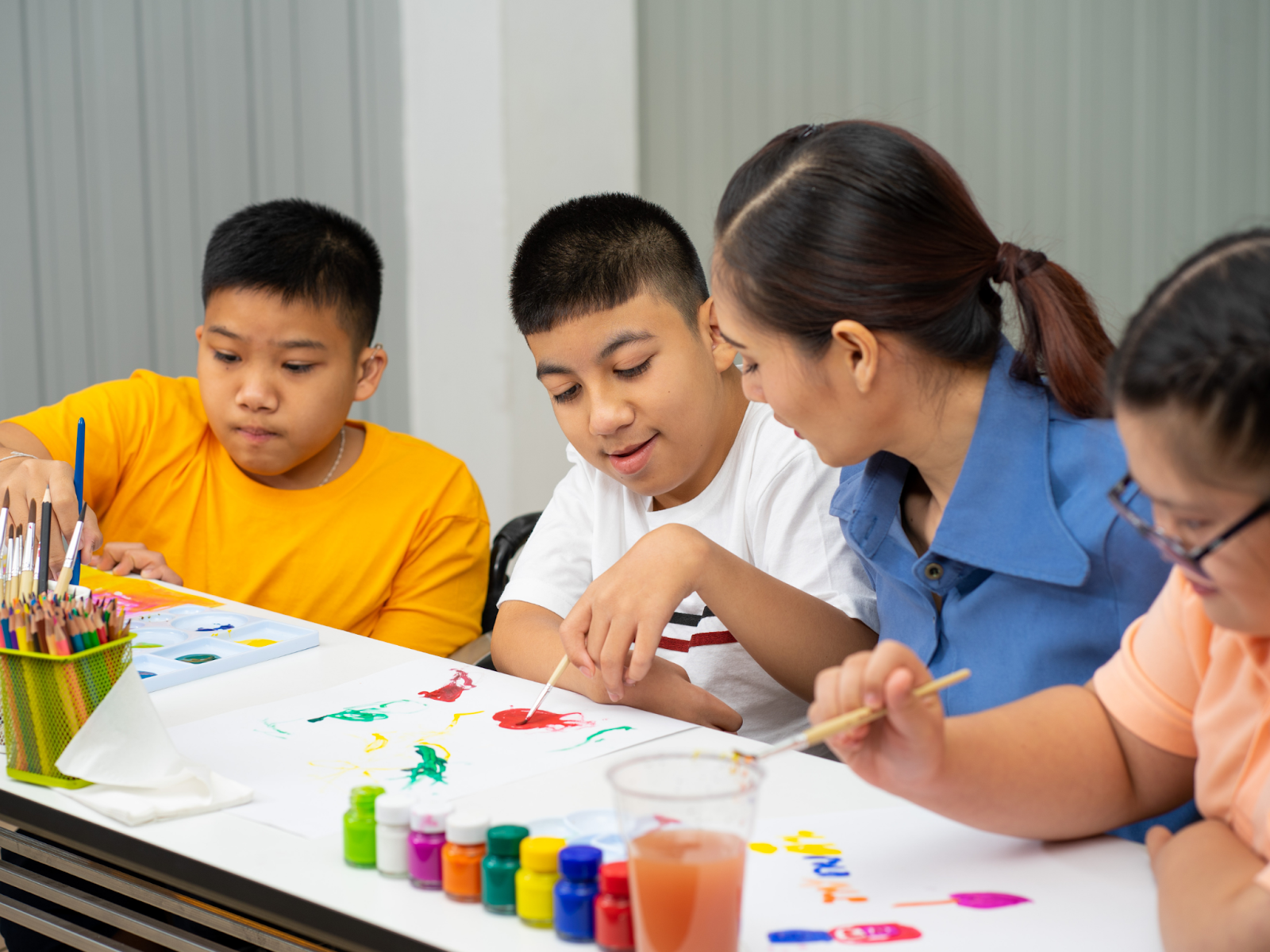 Four people sitting at a table painting together, one of whom is holding their arm in a “T-rex” position.