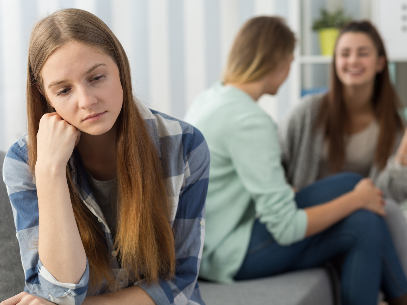Two girls laughing together while one sits by herself looking sad.