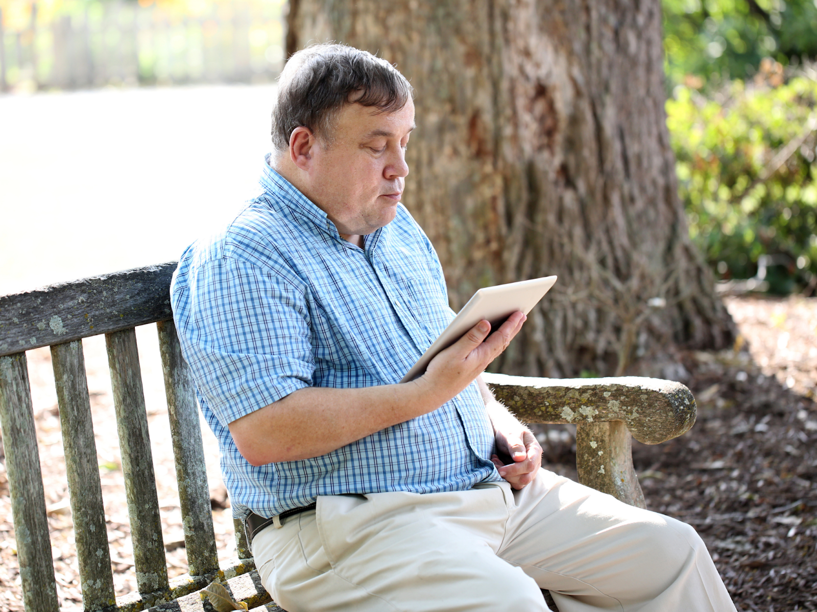 A man sitting on a park bench looking at a tablet.